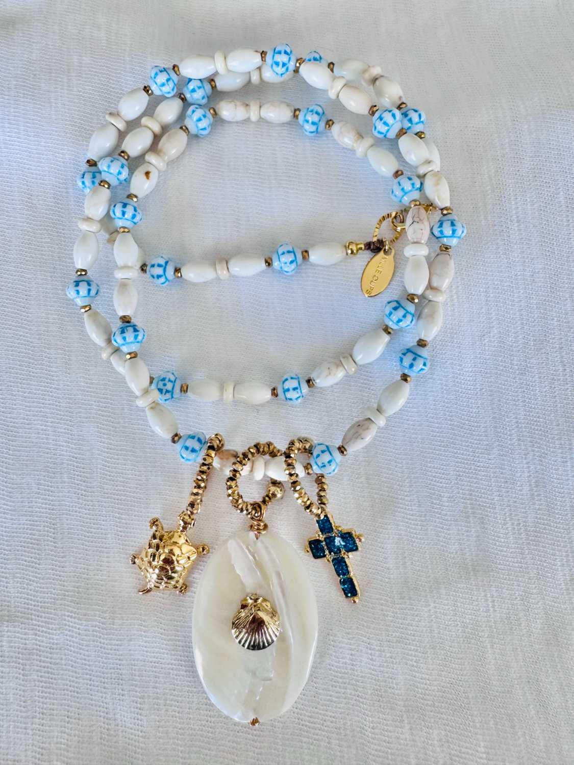 NOMAD coquillage nacre blanc bleu - Mademoiselle Oups Collier NOMAD blanc et bleu avec coquillage nacré, croix turquoise et charms dorés inspiration Riviera