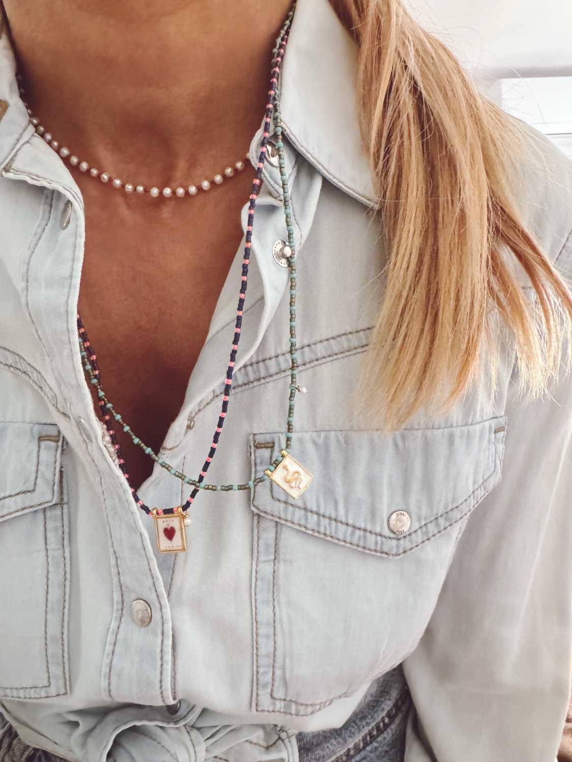 AMULET color collier scapulaire avec perles colorees avec chemise Accumulation de colliers AMULET colorés portés sur une chemise bleu clair, bijoux talismans dorés inspirés de l'été - Mademoiselle Oups
