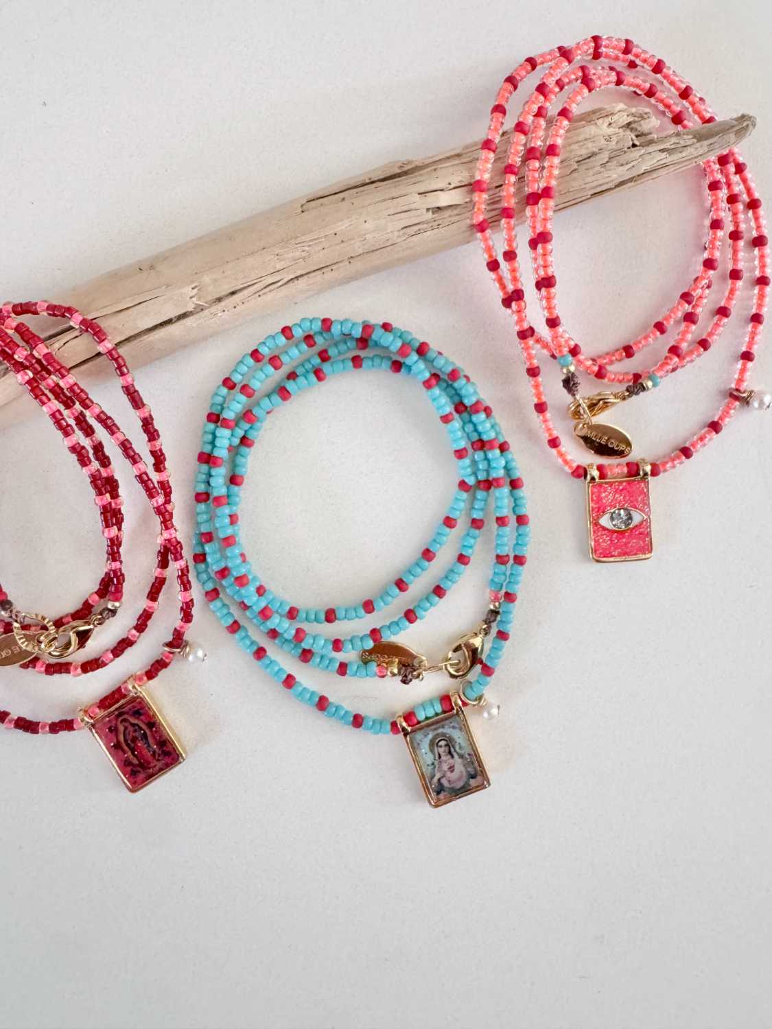 AMULET color colliers scapulaires colorés et bois flotte Capsule AMULET été 2026 composée de colliers de perles colorées et scapulaires émaillés dorés à l'or fin, présentés sur un bois flotté - Mademoiselle Oups