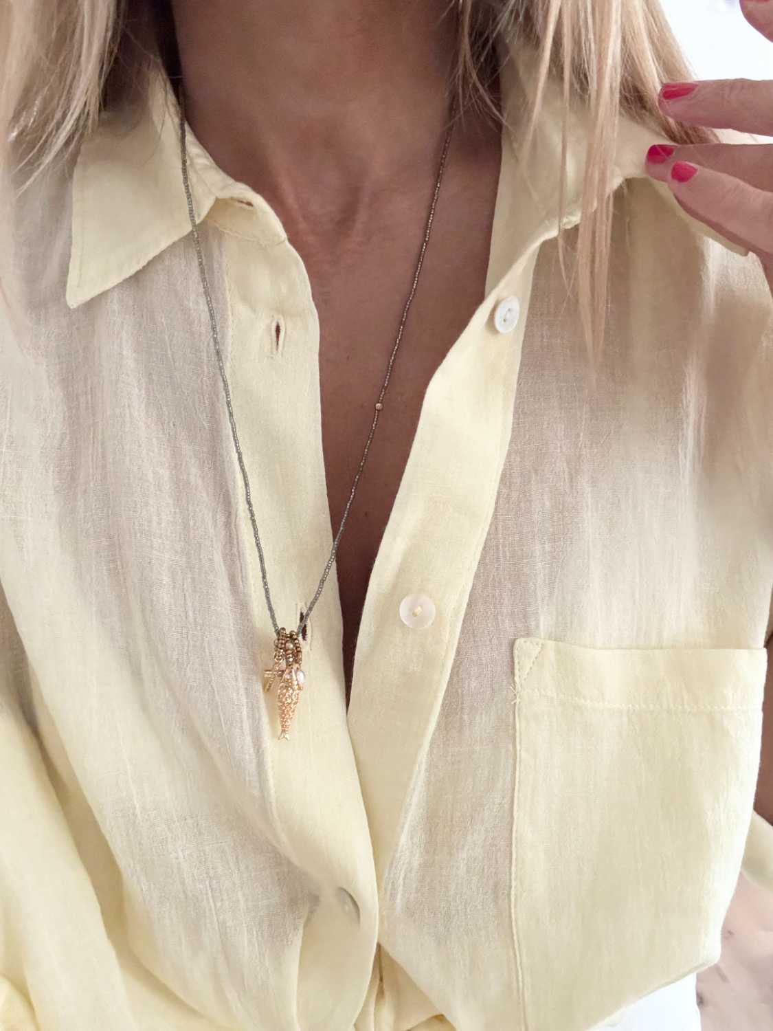 ICON-09-collier-poisson-porte-face-longueur Collier ICON 09 Mademoiselle Oups porté en longueur sur chemise en lin jaune pâle, collier talisman gris avec poisson doré