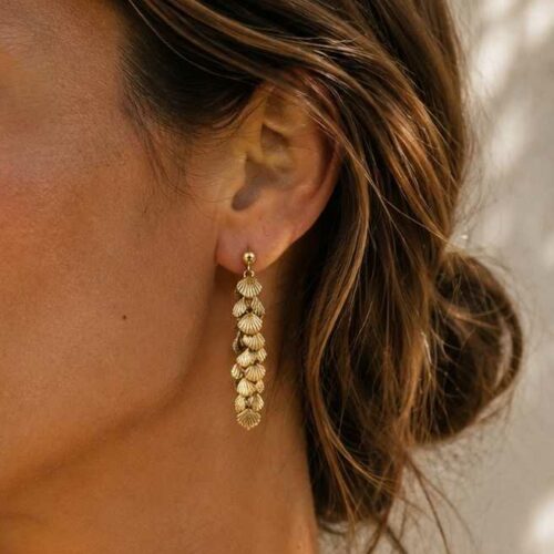 Boucles d’oreilles Calypso pendantes dorées à l'or fin 24K composées de petits coquillages dorés, porté par une femme brune fabrication française.
