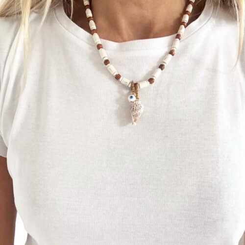 Collier ISLA en jade blanche et river stone et perles de bois avec pendentif coquillage naturel et œil protecteur porté sur un tshirt blanc – création artisanale Mademoiselle Oups