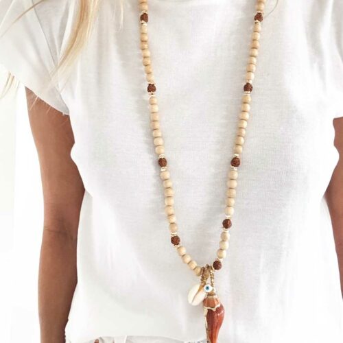 Sautoir OASIS en perles de bois beige, graines de Rudraksha, coquillage cauri, œil protecteur et coquillage naturel doré porté long sur tshirt blanc – création artisanale Mademoiselle Oups