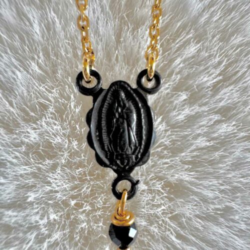Gros plan sur la médaille Vierge noire du collier chapelet NOX, reliée à une chaîne dorée et ornée d’une perle noire facettée.