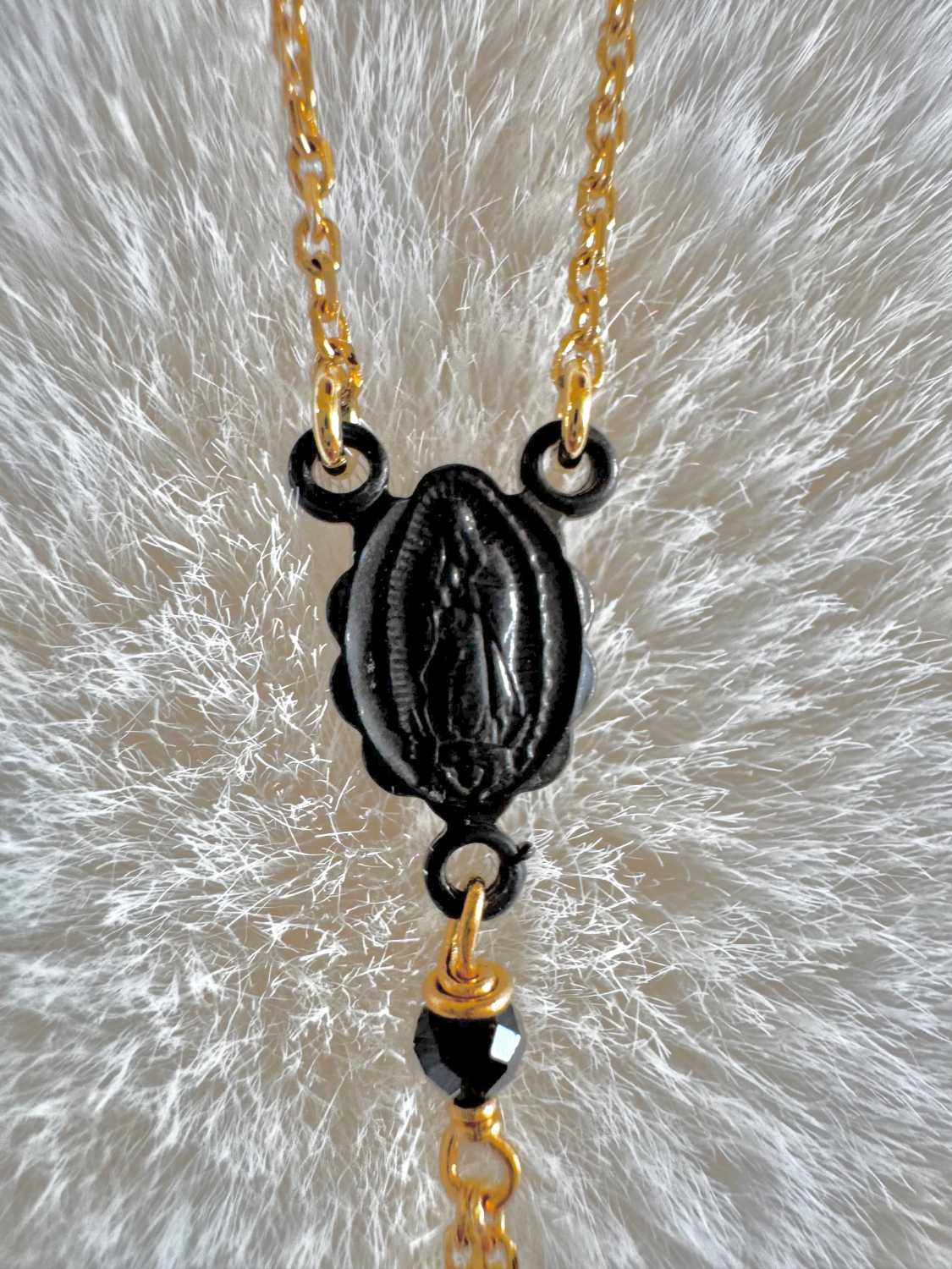 NOX-collier-chapelet-detail-medaille-vierge-metal-noir-mademoiselle-oups Gros plan sur la médaille Vierge noire du collier chapelet NOX, reliée à une chaîne dorée et ornée d’une perle noire facettée.