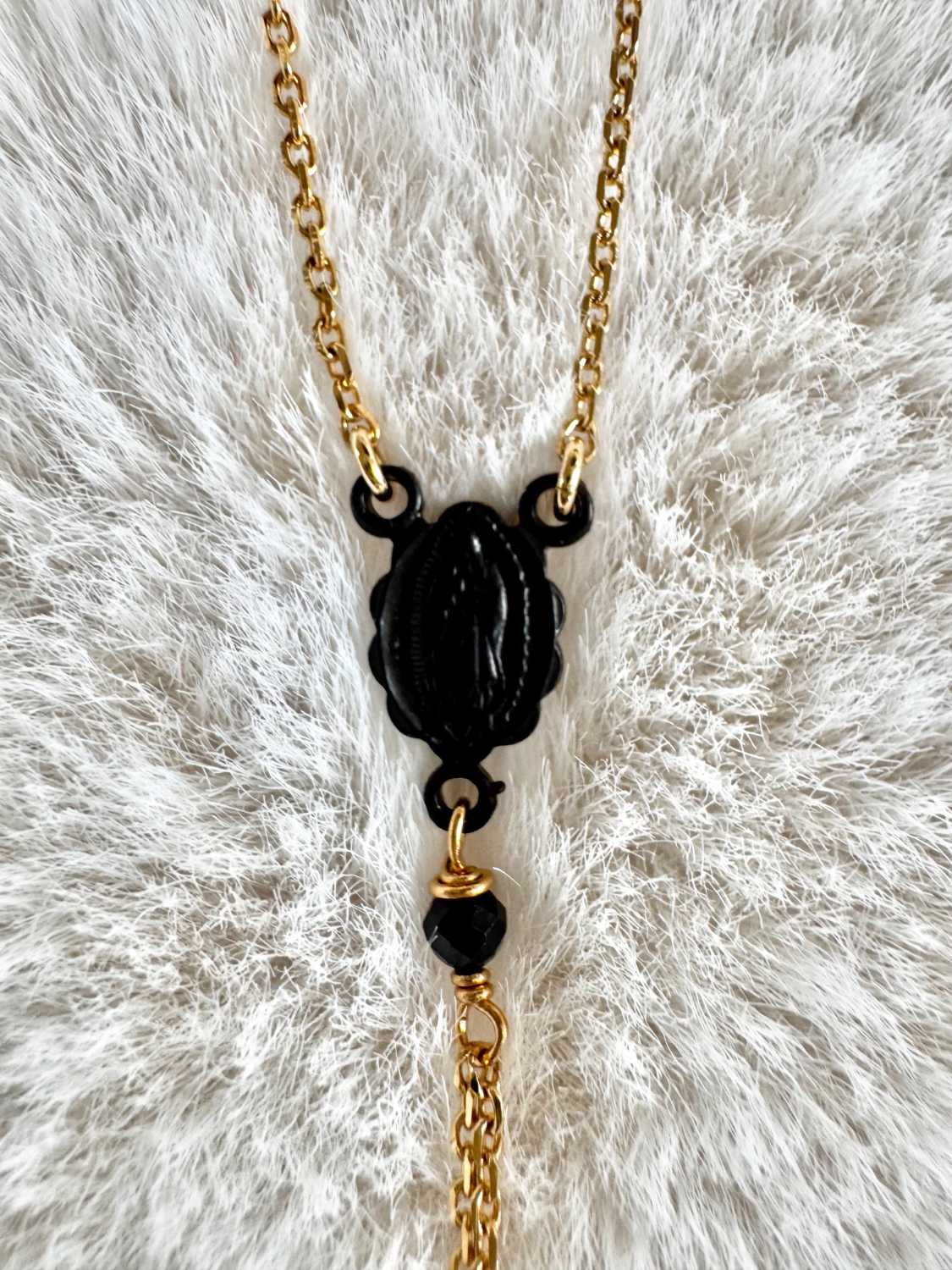 NOX-collier-chapelet-detail-vierge-metal-noir-chaine-doree-mademoiselle-oups Gros plan sur le madone central du collier chapelet NOX, avec chaîne dorée, perle noire facettée et chaînes pendantes.