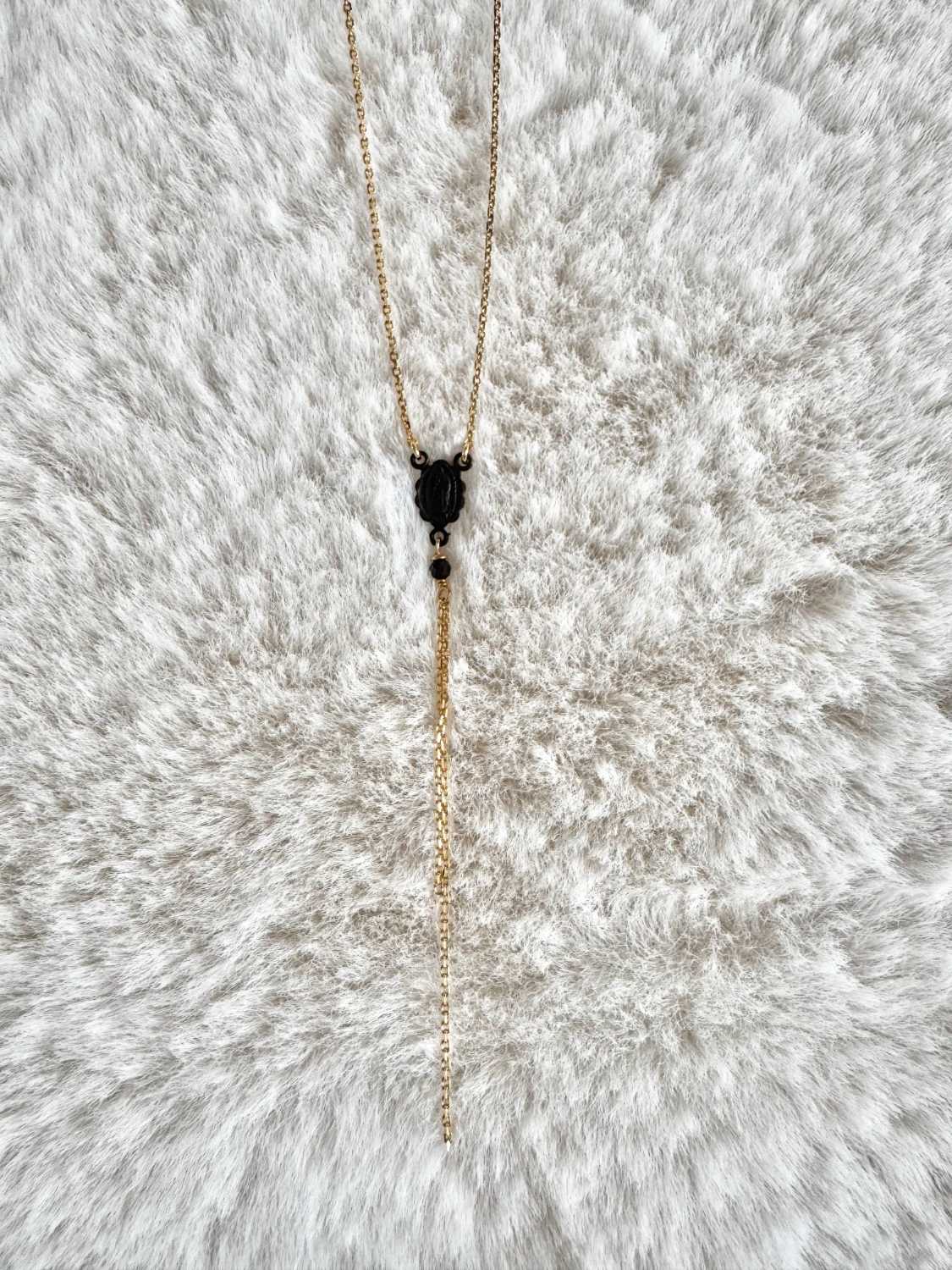 NOX-collier-chapelet-madone-noire-chaine-doree-mademoiselle-oups Collier chapelet NOX en fine chaîne dorée, avec vierge central et longues chaînes pendantes, présenté sur fond clair.