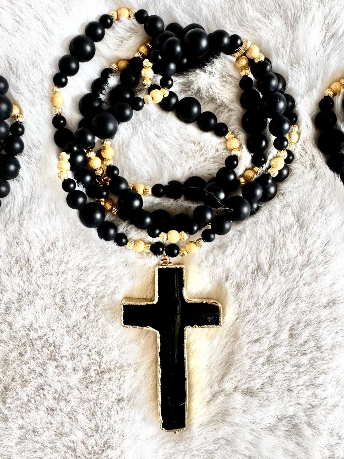 NOX-sautoir-croix-noire-onyx-perles-dorees-mademoiselle-oups Sautoir NOX en perles d’onyx noir mat de différentes tailles, perles dorées et grand pendentif croix noire bordée d’or, présenté sur fond clair.